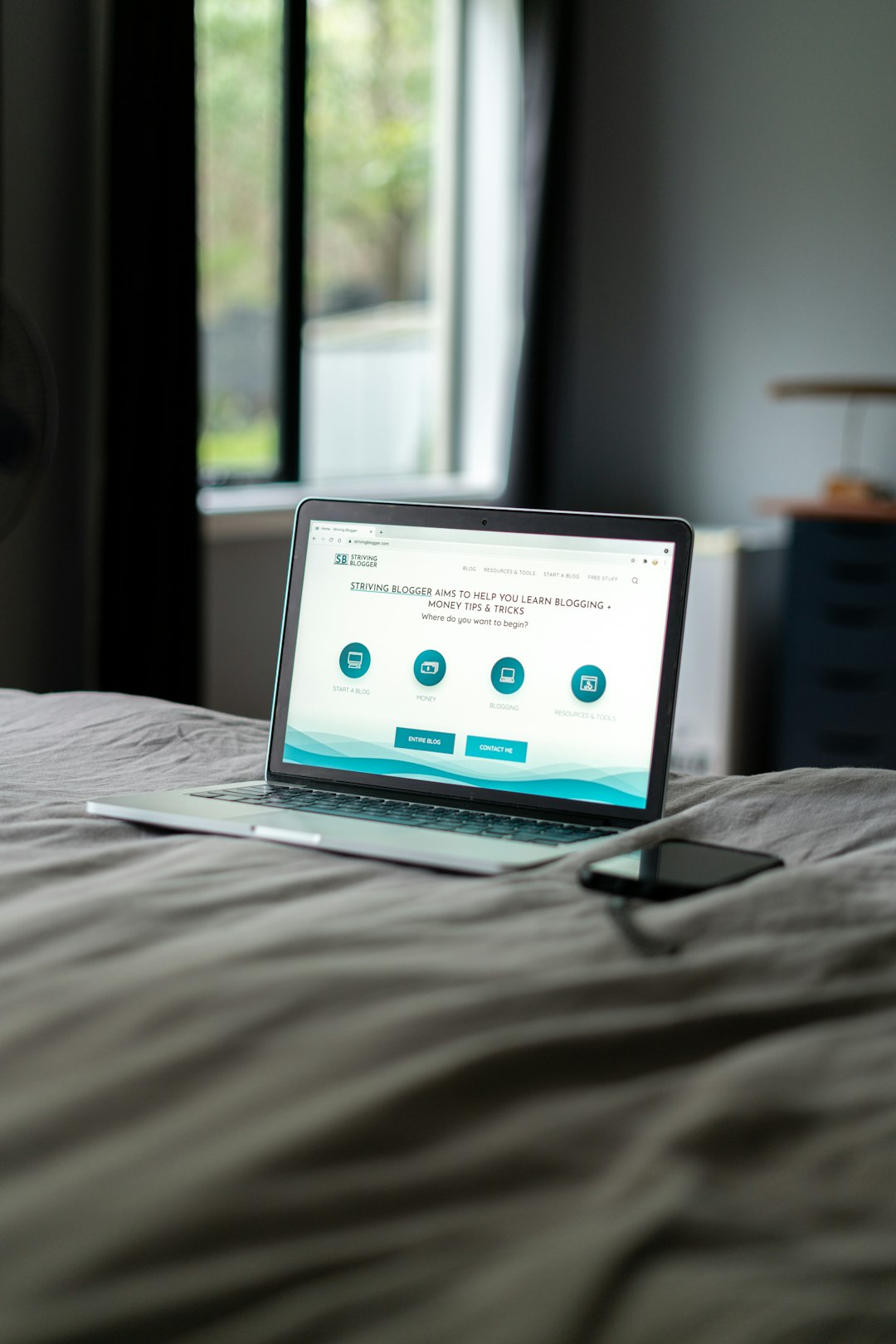MacBook on a bed with an iPhone next to it.